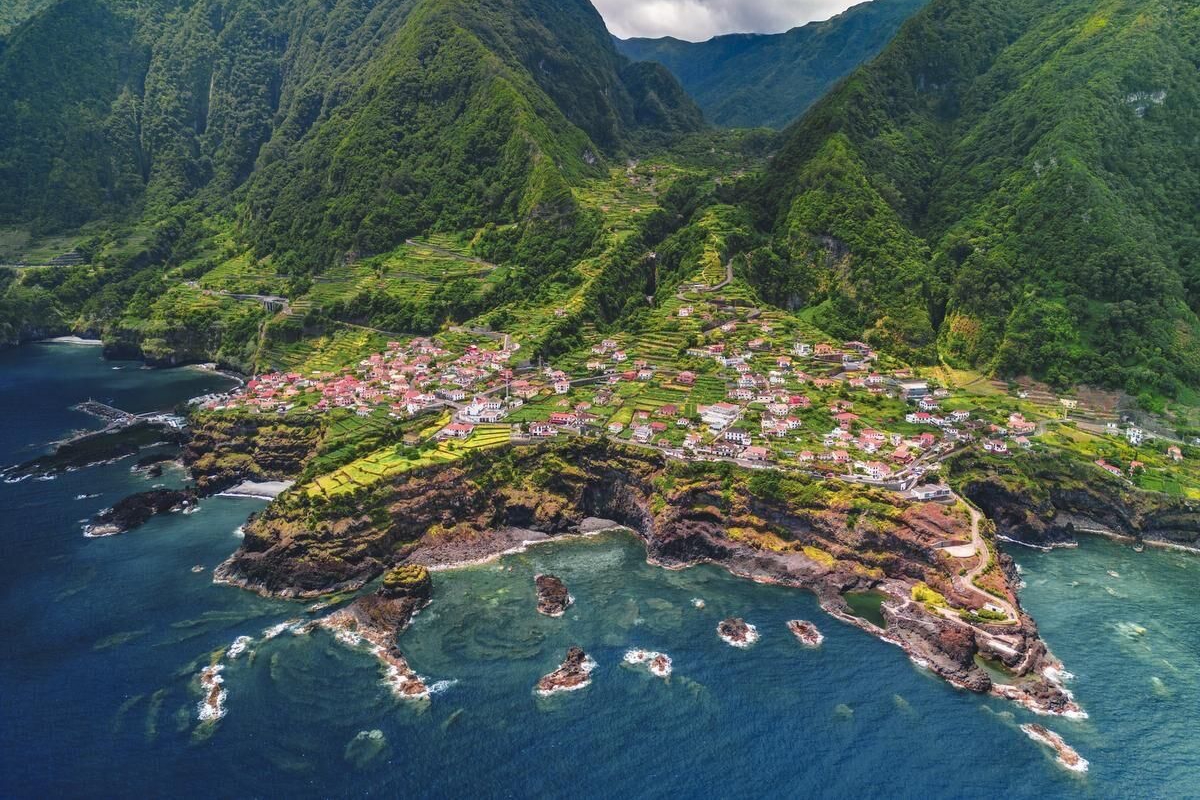 Aerial view of Madeira village on volcanic cliff surrounded by Atlantic ocean