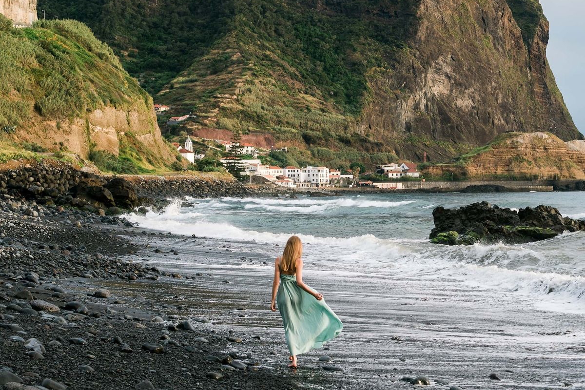 Woman walking on volcanic black sand beach in Madeira with dramatic cliffs