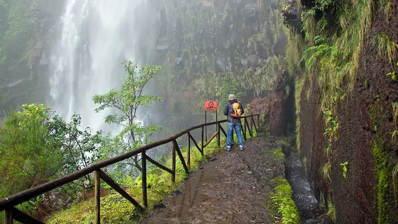 Hiker standing on a trail beside a waterfall in Madeira